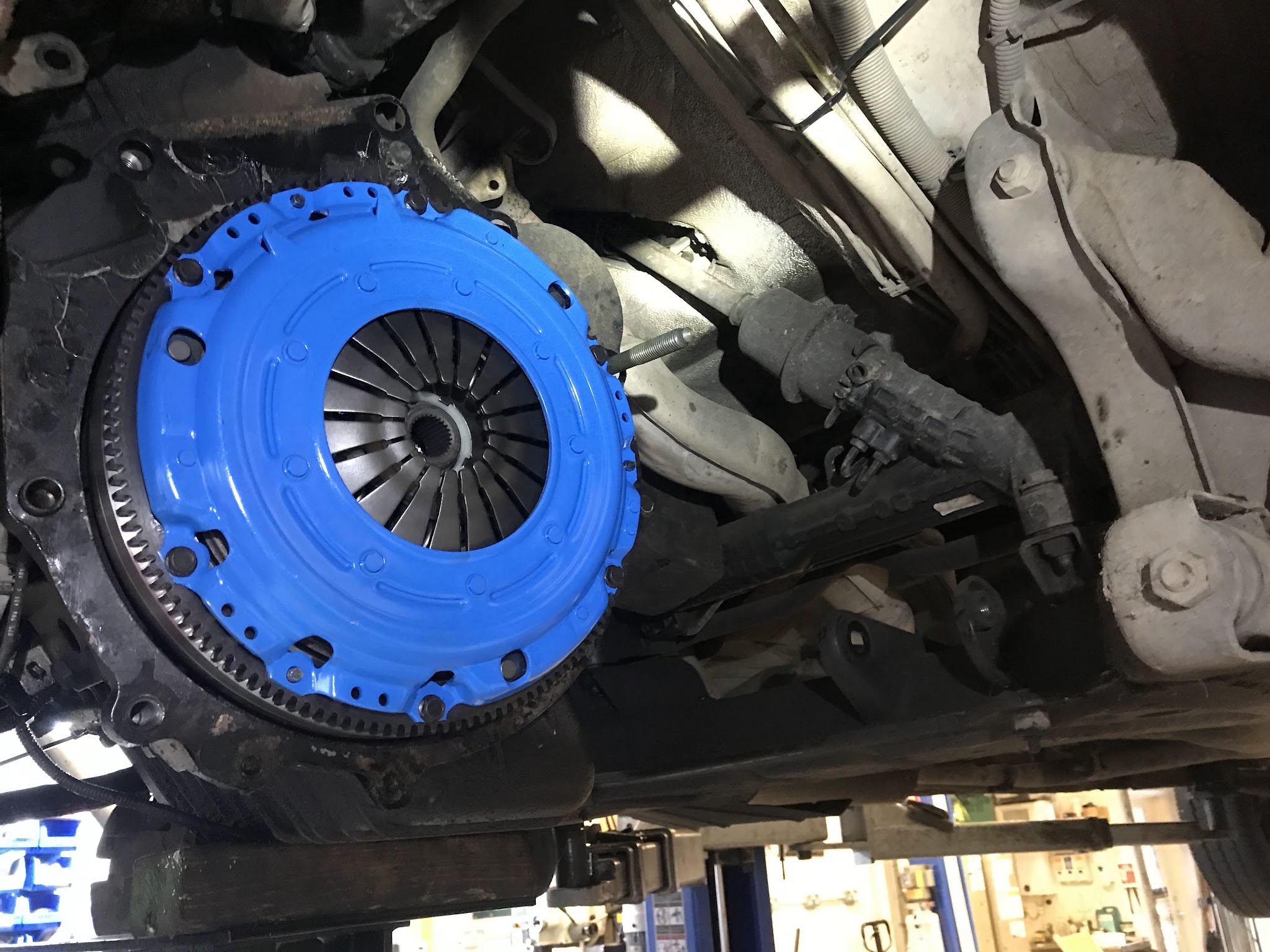 A bright blue clutch and flywheel fitted, seen from underneath the car