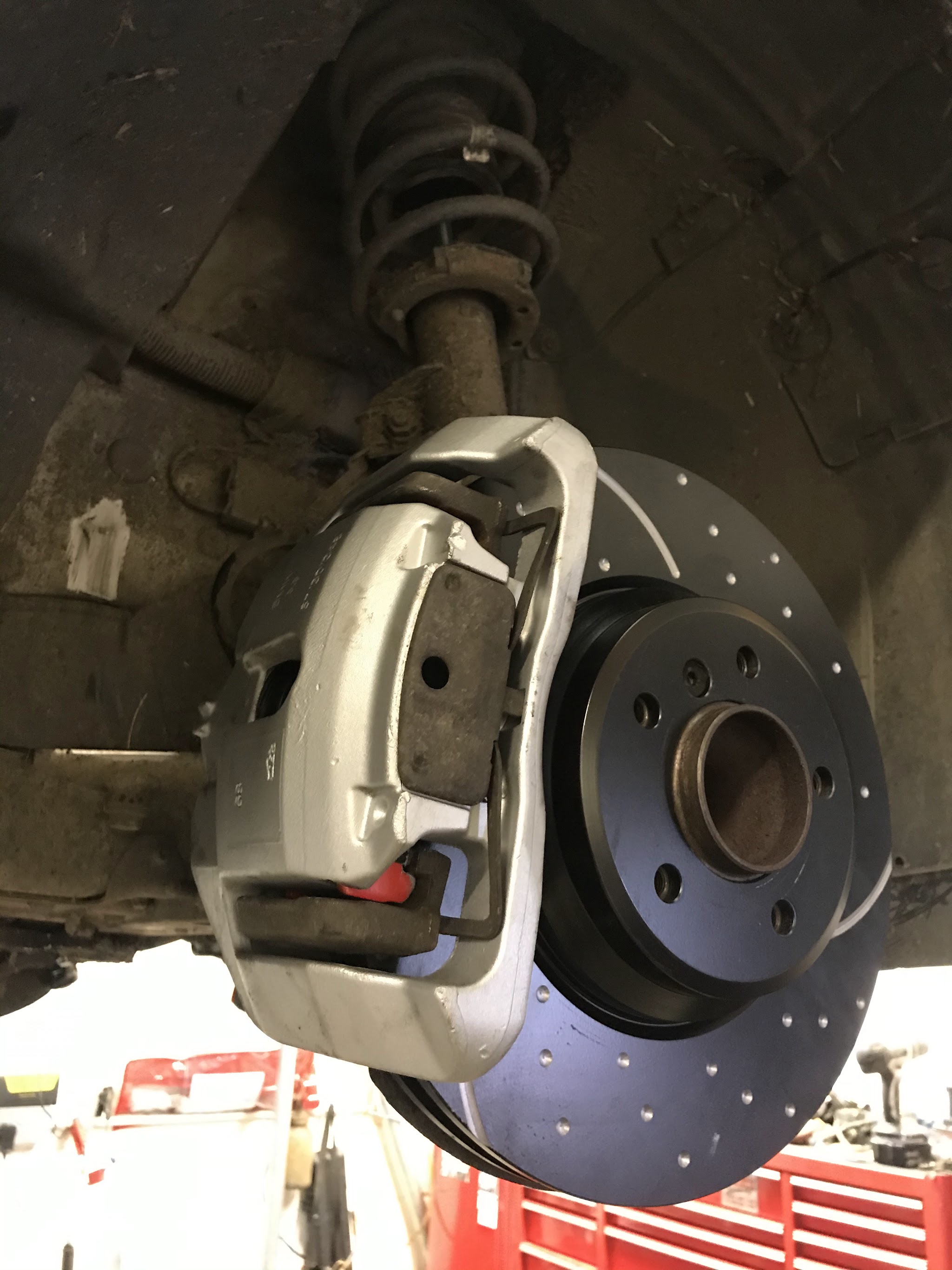 A new drilled brake disc and caliper fitted to a car on the ramp