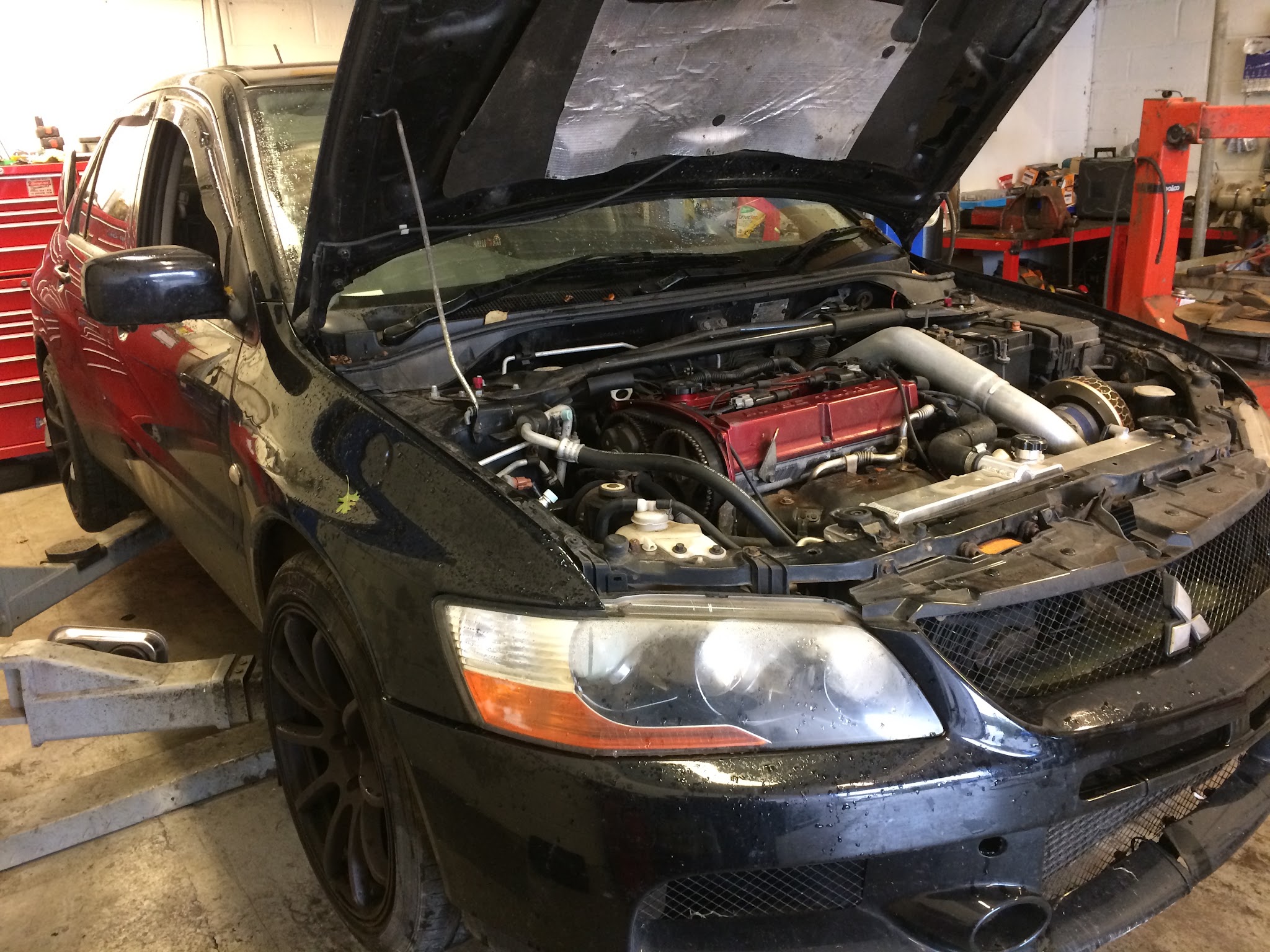 A black Mitsubishi Lancer Evo with its bonnet up in the workshop